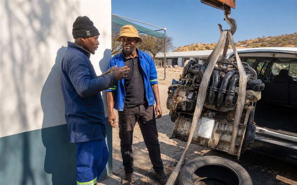 Triangle technicians working with a suspended vehicle engine