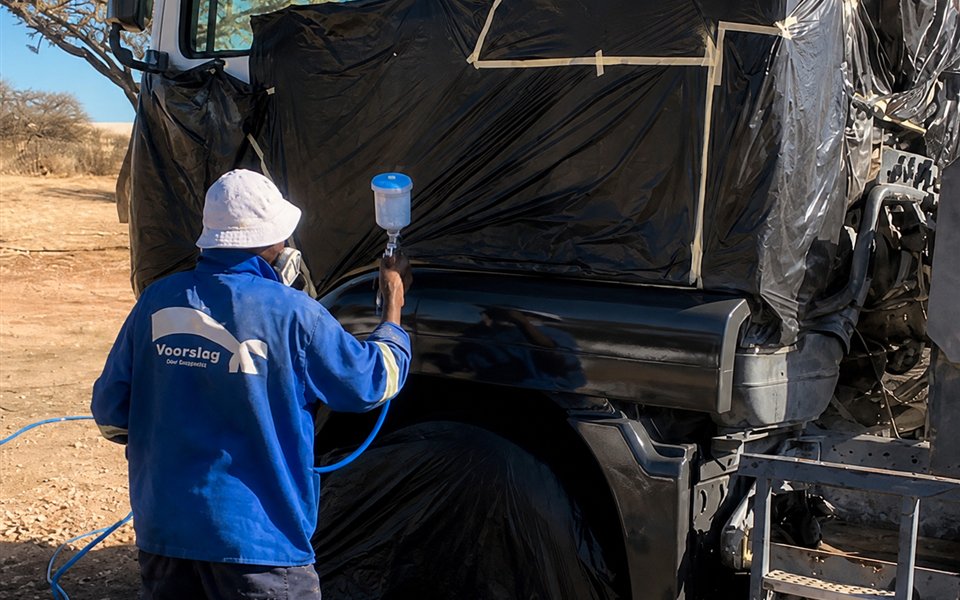Triangle technician spray-painting a masked truck panel